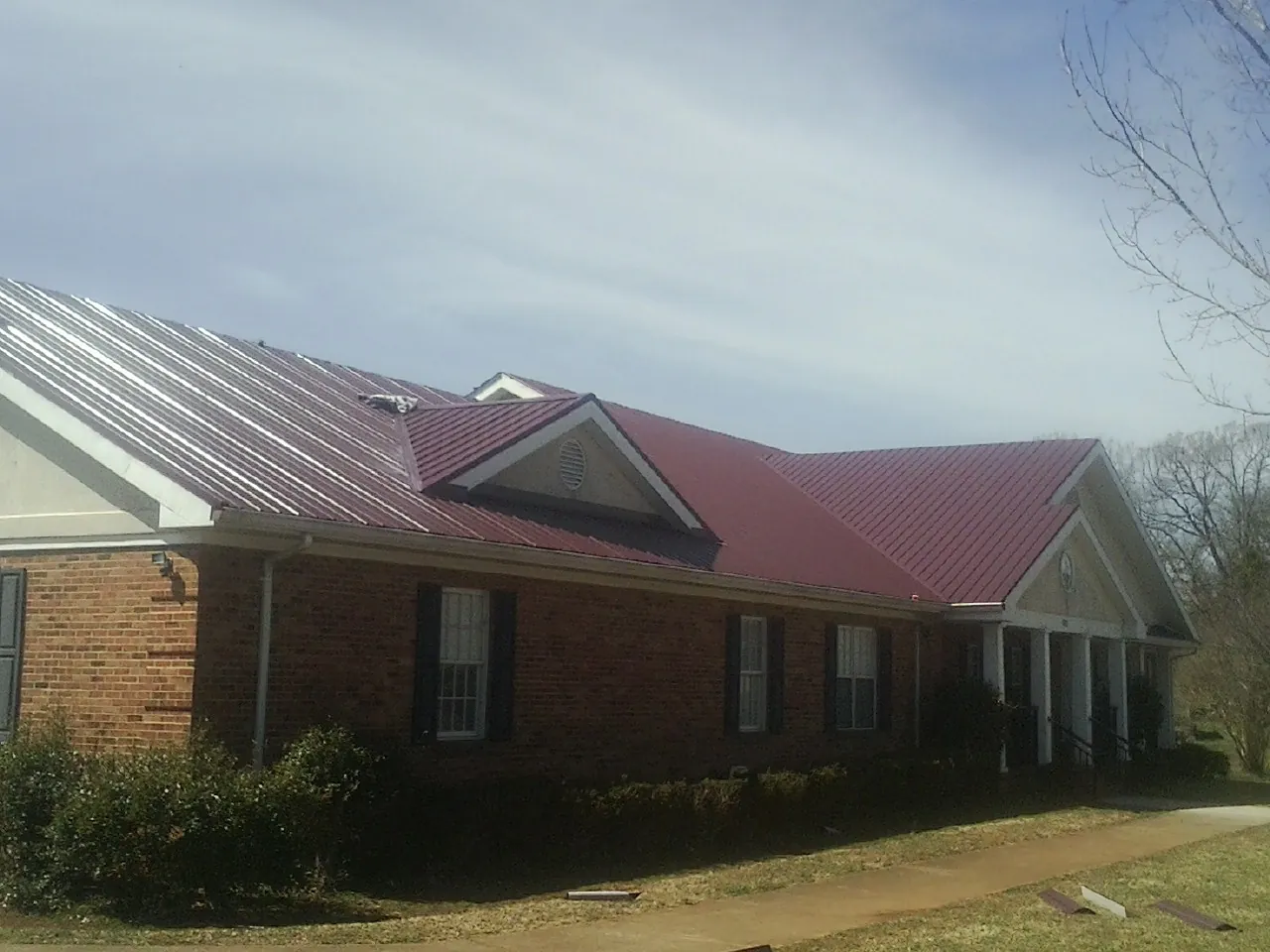 Red metal roof with gabled entries on a long brick building, from a Hail Damage Roof Repair job in East China