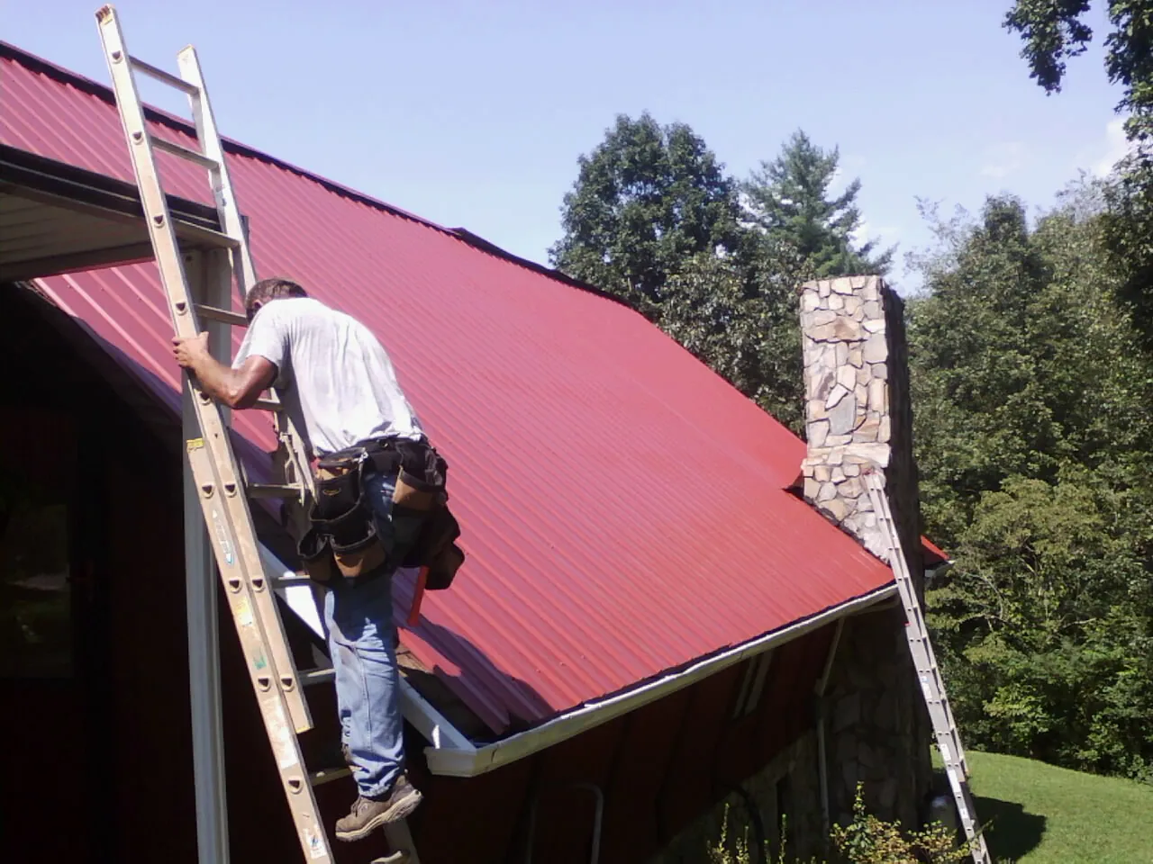 Roofer on a ladder beside a red metal roof and stone chimney in East China