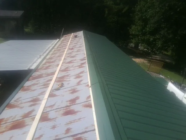 Old rusted panels beside newly installed green metal roofing — Wind Damage Roof Repair by Roofing Brothers in East China