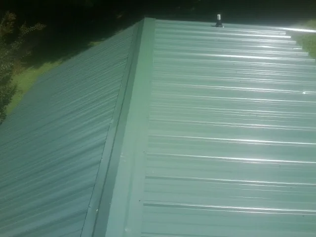 New green metal panels meeting at the ridge of a roof — Flat Roof Repair work by our crew in East China