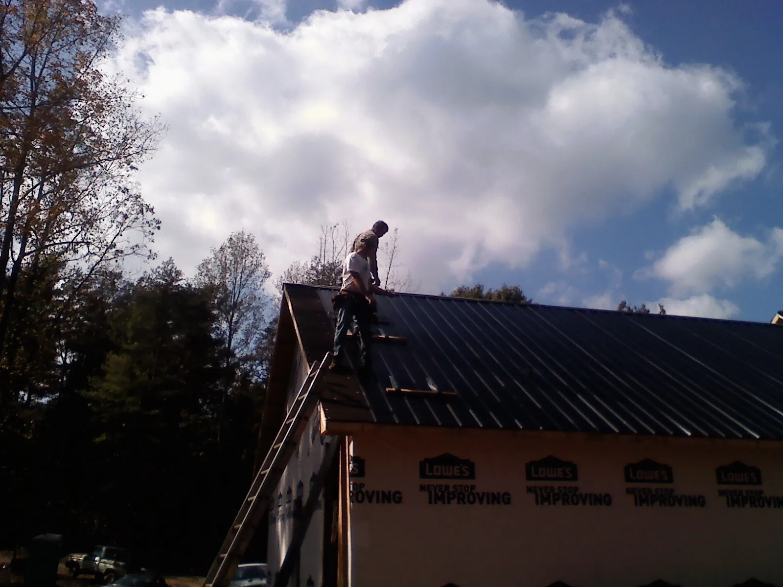 Roofer fastening dark metal panels high against a cloudy sky, from a Roof Inspection job in East China
